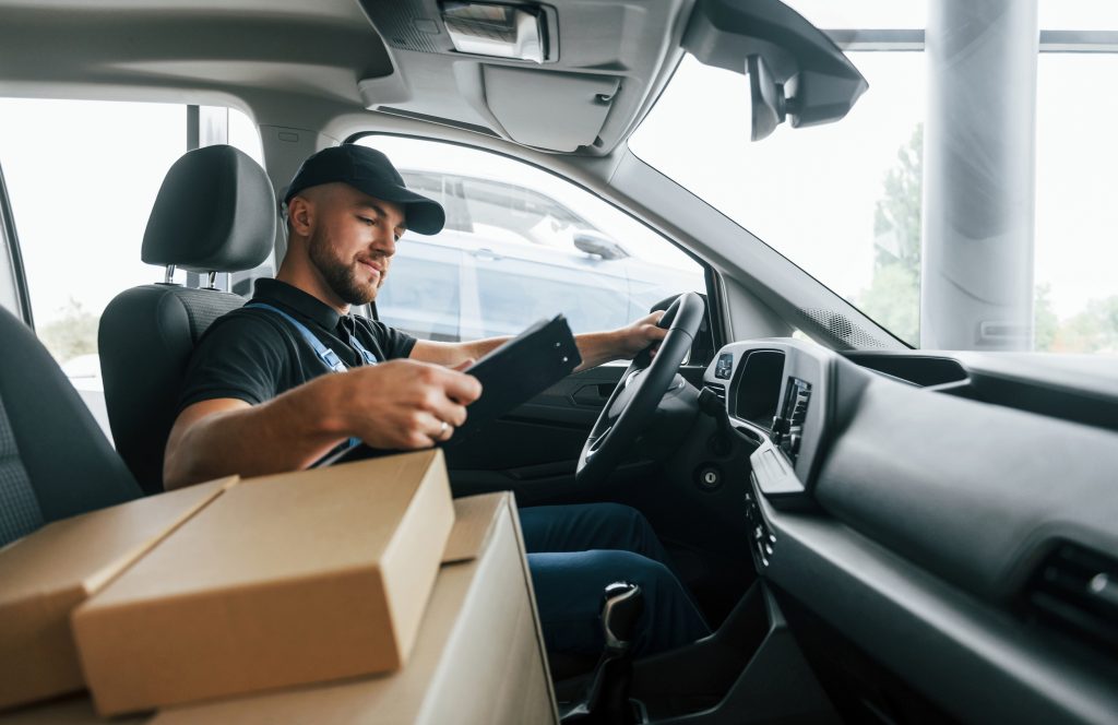 With vehicle. Delivery man in uniform is indoors with car and with order